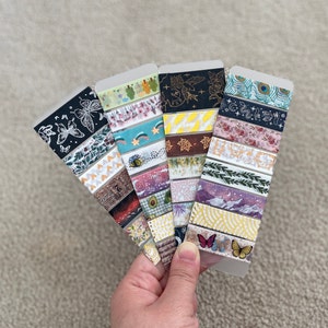 May include: A collection of colorful washi tapes with various patterns, including butterflies, stars, leaves, and geometric shapes. The tapes are displayed on a white background.