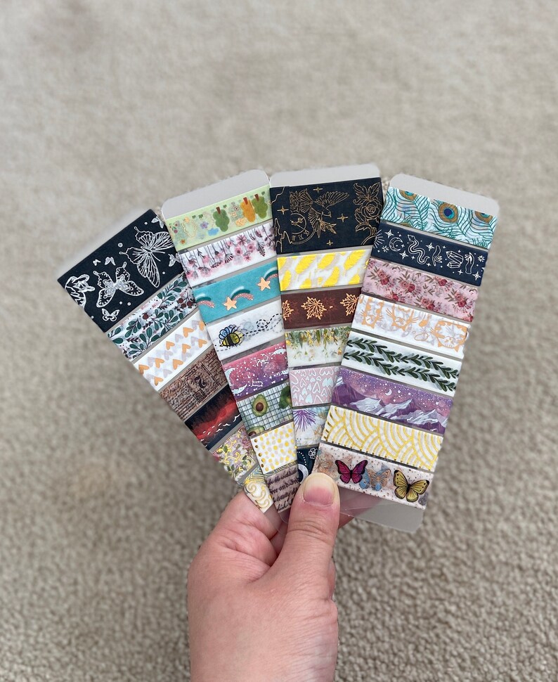 May include: A collection of colorful washi tapes with various patterns, including butterflies, stars, leaves, and geometric shapes. The tapes are displayed on a white background.