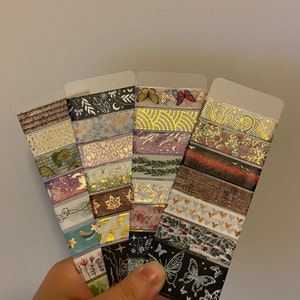 May include: A set of 10 decorative washi tapes featuring various patterns and designs, including butterflies, flowers, geometric shapes, and gold accents. The tapes are displayed on a clear plastic backing.