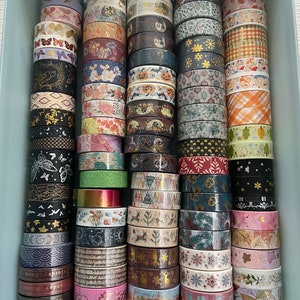 May include: A collection of colorful washi tapes in a light blue plastic container. The tapes feature various patterns, including floral, geometric, and animal prints.