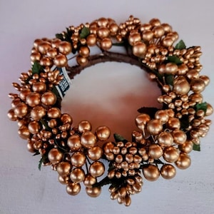 May include: A gold-colored wreath made of small, round berries and green leaves. The wreath is about 6 inches in diameter.