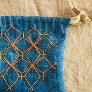 May include: A blue fabric drawstring bag with a geometric pattern of orange and yellow stitching.