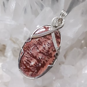 May include: A silver wire wrapped pendant featuring a red and white patterned stone. The stone is oval shaped and has a natural, organic look.