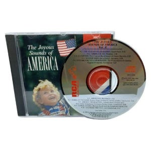 May include: A compact disc titled The Joyous Sounds of America Vol. II, featuring a cover with a child and an American flag. The disc surface lists nine tracks including The Star-Spangled Banner and America the Beautiful, with RCA branding.