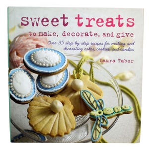 Puede incluir: Un libro de cocina titulado "Sweet Treats" con galletas decoradas en un plato de cristal. Las galletas incluyen galletas cameo glaseadas azules y blancas, galletas en forma de concha y una galleta de libélula. El libro dice "to make, decorate, and give".