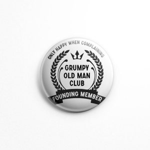 May include: A white button with the text "ONLY HAPPY WHEN COMPLAINING" around the edge. The center features "GRUMPY OLD MAN CLUB" with a crown and laurel wreath design. The bottom reads "FOUNDING MEMBER".