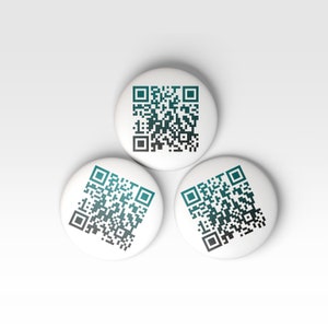 K&ouml;nnte beinhalten: Drei wei&szlig;e runde Kn&ouml;pfe mit schwarzen und t&uuml;rkisfarbenen QR-Codes darauf gedruckt.