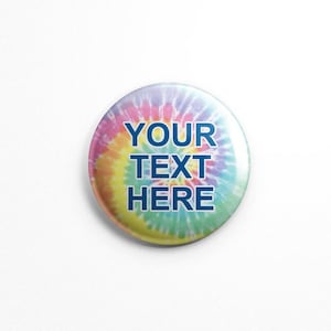 May include: A round button with a tie-dye pattern in shades of pink, yellow, blue, and green. The text "YOUR TEXT HERE" is printed in dark blue on the button.