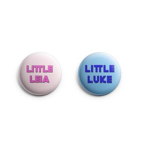 May include: Two round buttons with the text "LITTLE LEIA" on a pink button and "LITTLE LUKE" on a blue button.