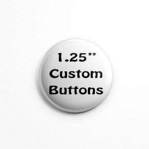 May include: A circular white button with black text that reads 1.25" Custom Buttons. The button has a smooth, glossy finish and a rounded edge, presenting a clear and legible display of the text centered on its surface.
