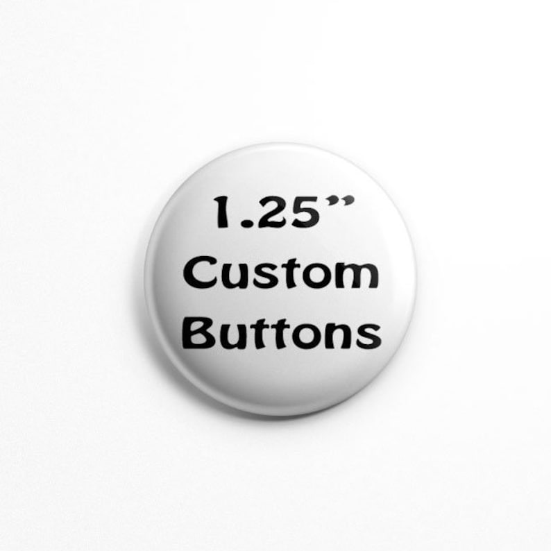 May include: A circular white button with black text that reads 1.25" Custom Buttons. The button has a smooth, glossy finish and a rounded edge, presenting a clear and legible display of the text centered on its surface.