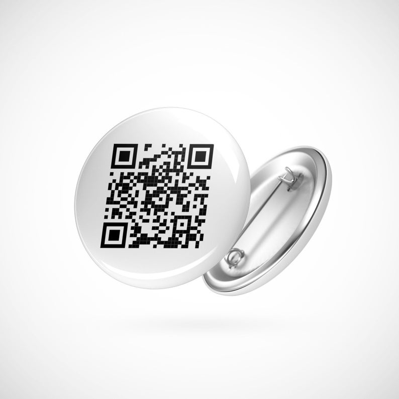 K&ouml;nnte beinhalten: Ein wei&szlig;er Knopf mit einem schwarzen QR-Code-Design. Der Knopf hat eine silberne Sicherheitsnadel.