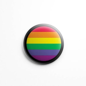 May include: A round button with a black border and a rainbow design. The rainbow has six stripes: red, orange, yellow, green, blue, and purple.