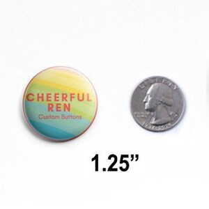 May include: A round pin-back button with a rainbow-colored background featuring the text CHEERFUL REN Custom Buttons in orange and white. The button is shown next to a US quarter for scale, with the text 1.25 inches indicating its diameter.