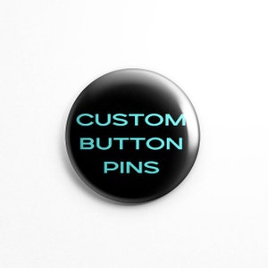 Puede incluir: Un pin redondo con un acabado negro brillante. El texto CUSTOM BUTTON PINS est&aacute; impreso en una fuente sans-serif de color azul claro y negrita en el centro del pin. El dise&ntilde;o presenta una superficie lisa y reflectante con un brillo.