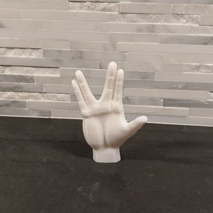 Peut inclure: Un modèle de main imprimé en 3D blanc faisant le salut Vulcain, un geste populaire de la franchise Star Trek.