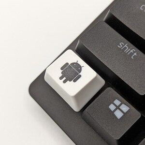May include: A black keyboard with a white key featuring the Android logo. The key is located next to a black key labeled "shift".