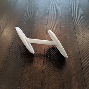 May include: A white dumbbell-shaped object with a round base on each end. The object is lying on a dark brown wooden floor.