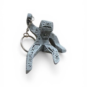May include: A gray, 3D-printed keychain in the shape of a stylized person. The figure is holding a silver key ring. The design features a textured, open-weave pattern throughout the body and limbs.