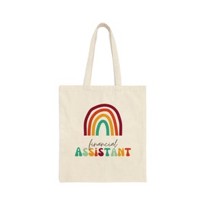 Op de afbeelding: Crèmekleurige draagtas met een regenboogontwerp en de woorden "financial assistant" in kleurrijke, retro-stijl letters. De tas heeft twee handvatten en is gemaakt van een stevige stof, geschikt voor het dragen van boeken, boodschappen of andere items.