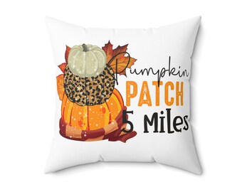 May include: White square pillow with a fall-themed design. The design features stacked pumpkins, fall leaves, and the text "Pumpkin Patch 5 Miles". The pumpkins are orange, white, and leopard print. A scarf is wrapped around the bottom pumpkin.
