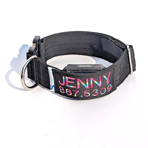 Op de afbeelding: Een zwarte nylon halsband voor huisdieren met een zilverkleurige metalen D-ring, een zwarte plastic gesp en een rechthoekige patch met de naam JENNY en het nummer 867.5309 geborduurd in meerkleurig regenbooggaren op een zwarte achtergrond.
