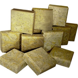 May include: A stack of handmade soap bars with a speckled green and brown colour. The bars are square shaped and have a marbled appearance.