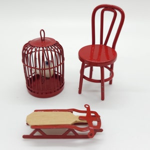 May include: Miniature red painted birdcage with a small white bird inside, a red chair, and a red and wood sled. The objects are set against a white background. The birdcage is round with vertical bars and a small handle.