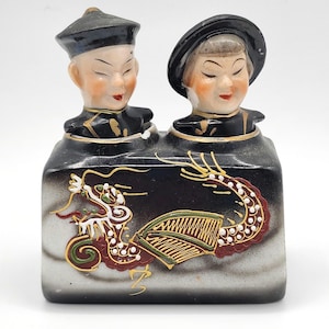 May include: A ceramic inkwell featuring two sculpted figures wearing black hats and traditional attire. The rectangular base is black with a white gradient and displays a hand-painted dragon motif in red, green, and gold with white dot accents.