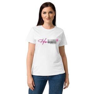 May include: White t-shirt with the word "Her" in a cursive pink font, accompanied by a color block design and the text "The future is female" in a small, gray font. The model is wearing blue jeans.