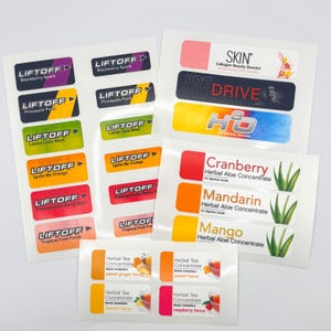 May include: A collection of product labels with various flavors and brands. The labels feature text such as "LIFTOFF," "SKIN," and "CR7 DRIVE." Colors include purple, green, orange, and red. The labels are for herbal tea concentrate and fitness drinks.