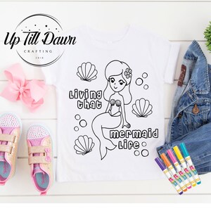 May include: A white t-shirt with a black and white outline of a mermaid with the text "Living that mermaid life".