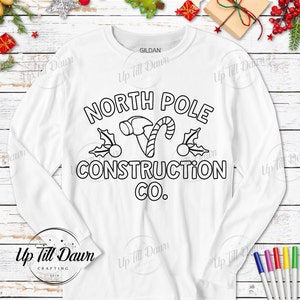 Op de afbeelding: Witte longsleeve t-shirt met een zwarte omtrek van een hamer, snoepstok, hulst en de tekst "North Pole Construction Co."