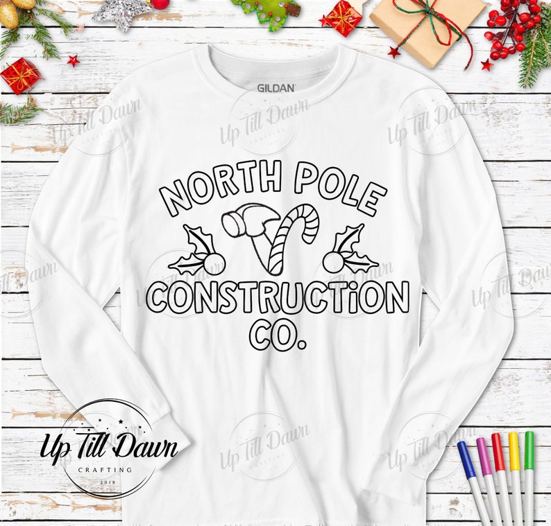 Op de afbeelding: Witte longsleeve t-shirt met een zwarte omtrek van een hamer, snoepstok, hulst en de tekst "North Pole Construction Co."