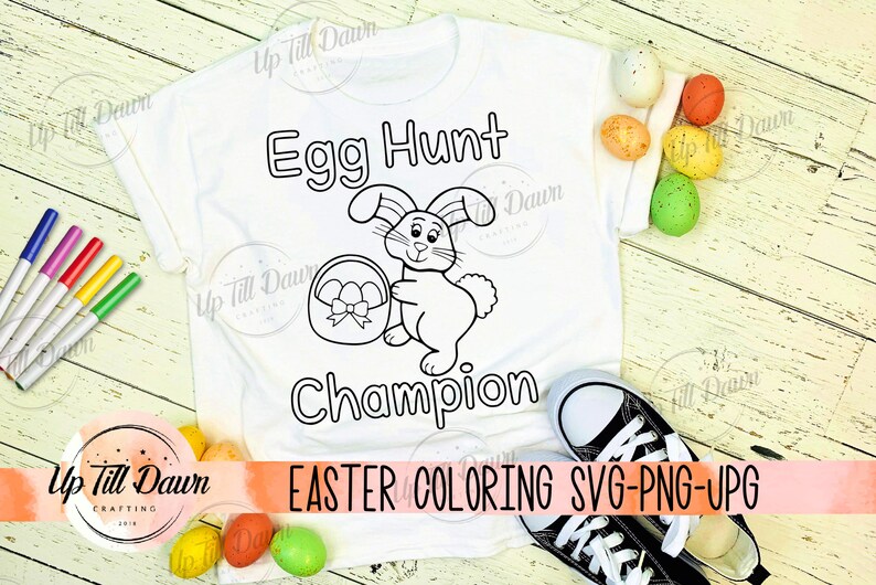 May include: A white t-shirt with a black and white outline of a bunny holding a basket of eggs. The text "Egg Hunt Champion" is written above the bunny. The text "EASTER COLORING SVG-PNG-UPG" is written below the bunny.