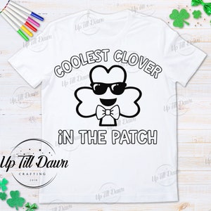 Puede incluir: Una camiseta blanca con un dise&ntilde;o en blanco y negro de un tr&eacute;bol con gafas de sol y una pajarita. El texto "COOLEST CLOVER IN THE PATCH" est&aacute; impreso en la camiseta.