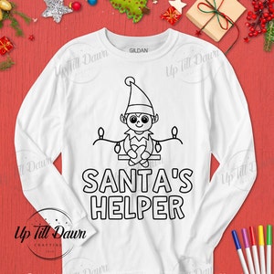 Op de afbeelding: Wit langarm shirt met een zwarte omtrek van een elf die op een tak zit met lampjes. De tekst "SANTA'S HELPER" is onder de elf gedrukt.