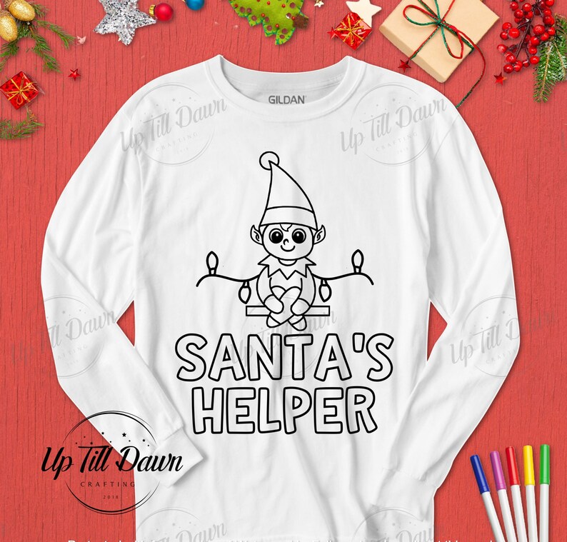 Op de afbeelding: Wit langarm shirt met een zwarte omtrek van een elf die op een tak zit met lampjes. De tekst "SANTA'S HELPER" is onder de elf gedrukt.