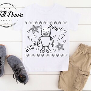 May include: A white t-shirt with a black and white robot design. The robot has the words "Beep!" and "Bop!" next to it. There are also stars and lightning bolts on the shirt.