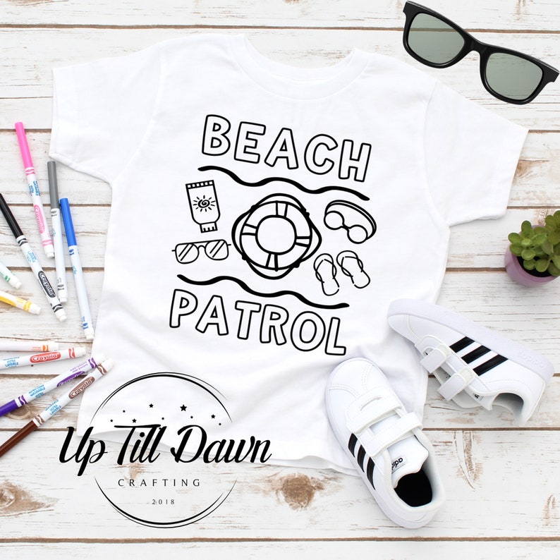 May include: A white t-shirt with a black outline of a life preserver, sunglasses, flip-flops, and sunscreen. The text "Beach Patrol" is written in black above the outline. The shirt is on a white wooden surface with a pair of white sneakers with black stripes.