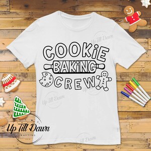 Op de afbeelding: Een wit T-shirt met een zwart-wit ontwerp met de tekst "Cookie Baking Crew". Het ontwerp bevat een deegroller, een koekje en een peperkoekman.