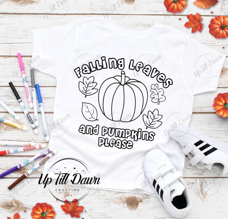 Puede incluir: Una camiseta blanca con un contorno en blanco y negro de una calabaza y hojas. El texto "Falling Leaves and Pumpkins Please" est&aacute; escrito en negro. La camiseta est&aacute; sobre una superficie de madera con hojas de oto&ntilde;o.