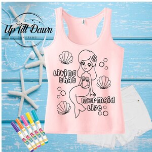 May include: A pink tank top with a black outline of a mermaid, seashells, and the text "Living that mermaid life".