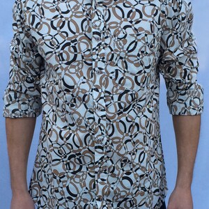 Può includere: Una camicia bianca a maniche lunghe con un motivo geometrico marrone e nero di cerchi intrecciati.