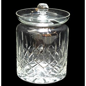 May include: A clear glass jar with a lid. The jar has a diamond-cut pattern on the lower portion and a smooth, cylindrical upper section. The lid has a small, round knob. The jar is likely used for storage.