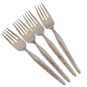 May include: Five silver forks with tines and handles. The handles are decorated with a floral rose pattern. The forks are arranged diagonally against a white background. The forks are made of metal.