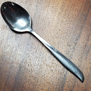 May include: A silver spoon with a star design on the handle. The spoon is on a wooden surface.