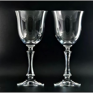 May include: Two clear glass wine glasses with a tall, slender stem and a wide bowl. The glasses are empty and have a polished, elegant look.