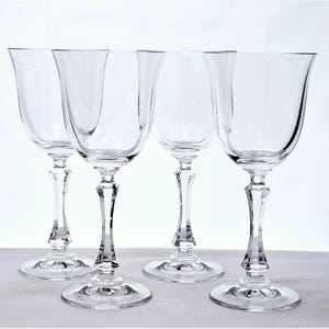 May include: Set of four clear glass wine glasses with a tall, slender stem and a wide bowl. The glasses are arranged in a row on a white surface.