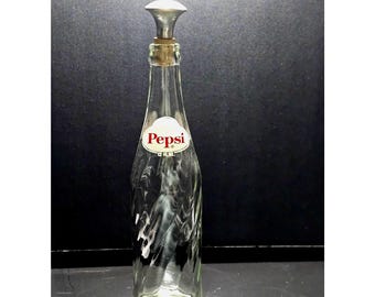May include: A clear glass Pepsi bottle with a swirling textured design. The bottle features a white oval label with the red text Pepsi and 12 FL. OZ. printed below. It is topped with a cork stopper and a silver-colored metal cap.